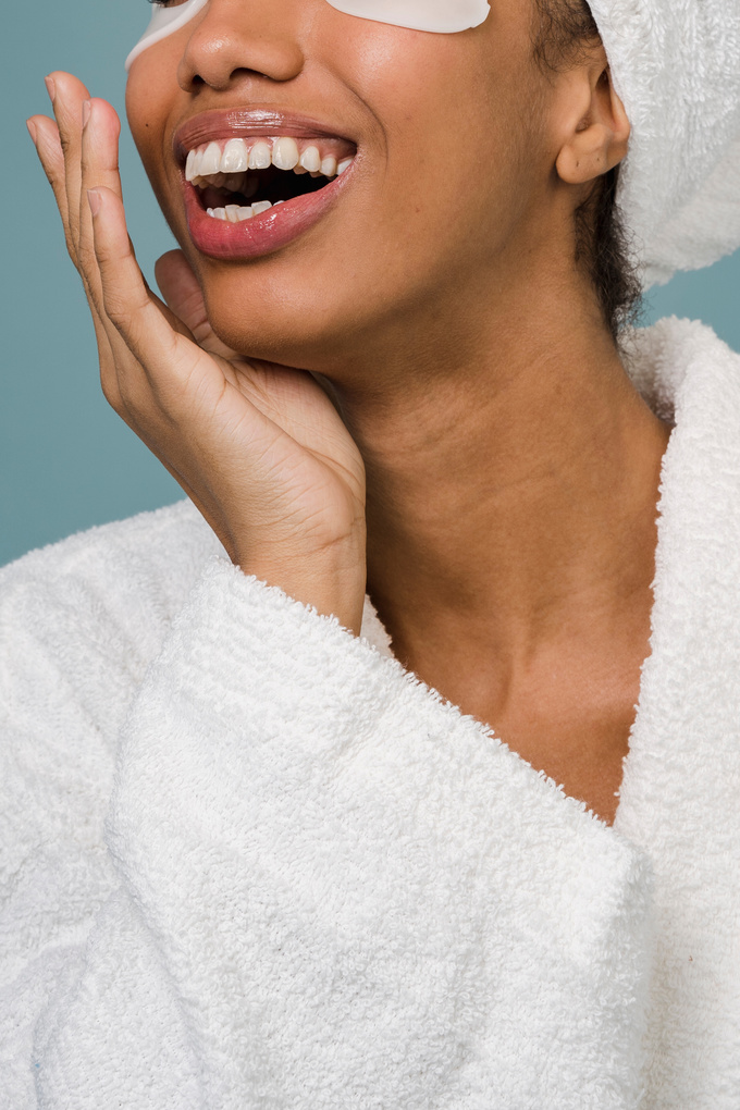 Delighted African American woman laughing during skin care routine after bath