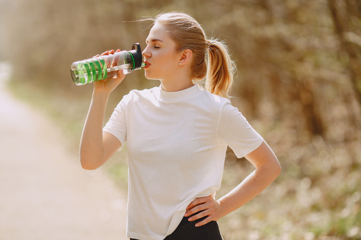 Woman in White Crew Neck T-shirt Drinking from Green Plastic Bottle